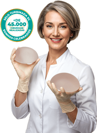 Imagem de uma mulher branca de cabelos escuros siliconada apontando para os seios com um sutiã rosa claro