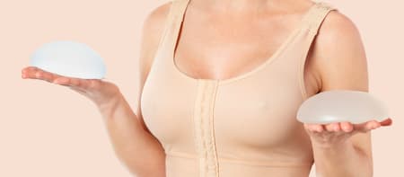 Mulher usando sutiã cirúrgico e segurando próteses de silicone